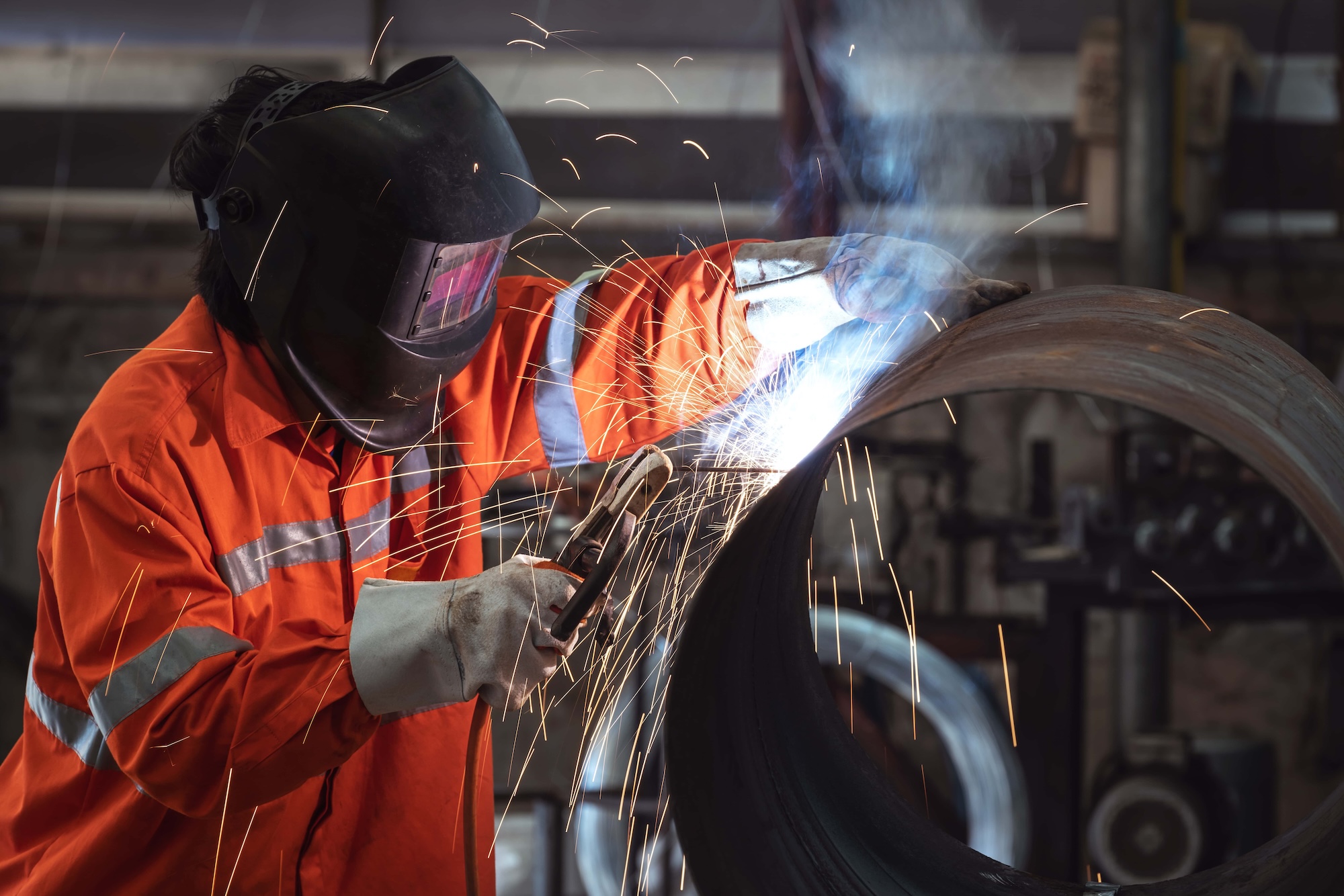 a worker with protective mask welding metal pipe in a factory