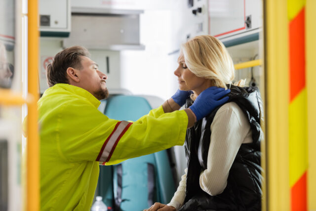 Side view of paramedic in latex gloves checking middle aged patient with hypertension in emergency vehicle, stock image