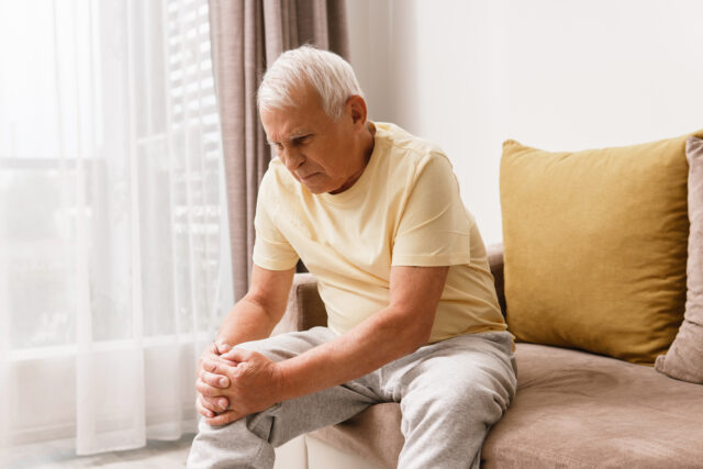 Senior man suffering from pain in his knee at home. Concept of problems with joint like arthritis.