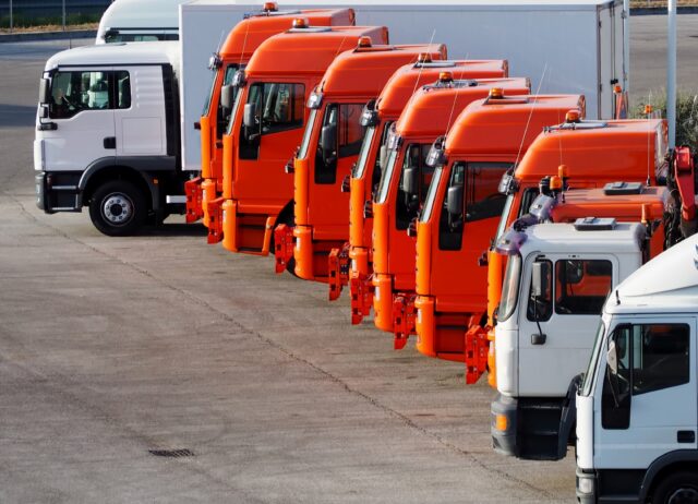 Orange trucks and white trucks lined up in a parking lot of a transport and shipping company, ready to go.