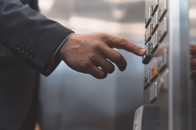 Man hand office worker in a business suit press the elevator button with his finger. Businessman in an office center elevator interior.